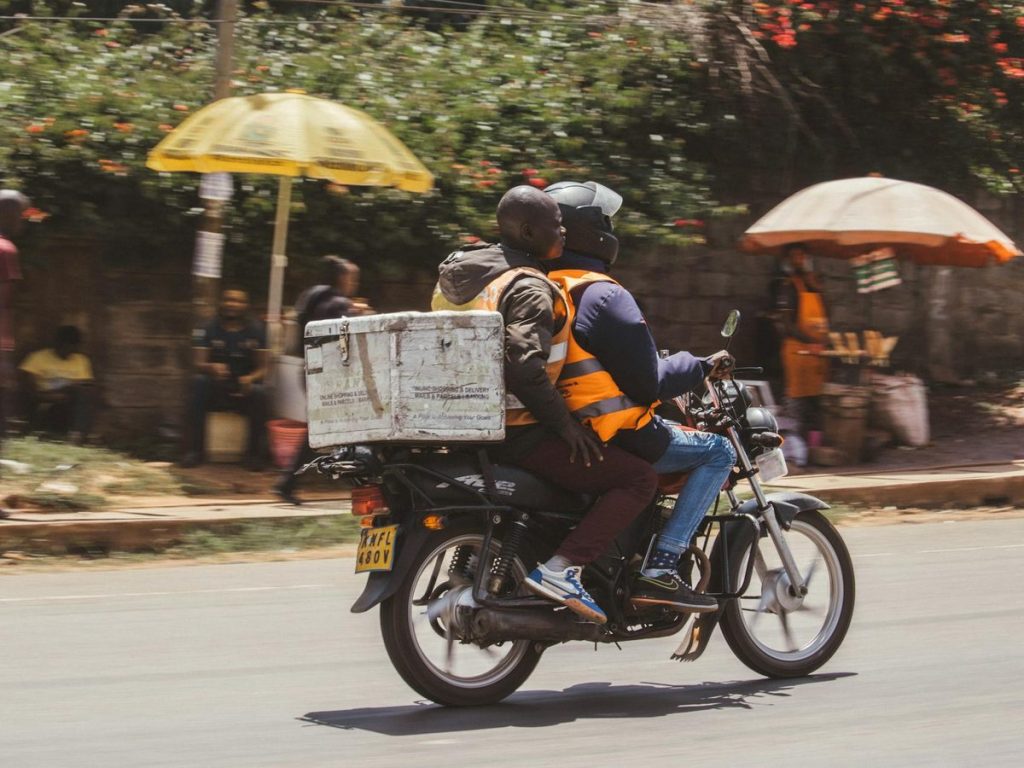 A Haraka Express delivery rider on a motorcycle speeding through Nairobi streets with a packed food delivery bag, ready to bring fresh meals to your door